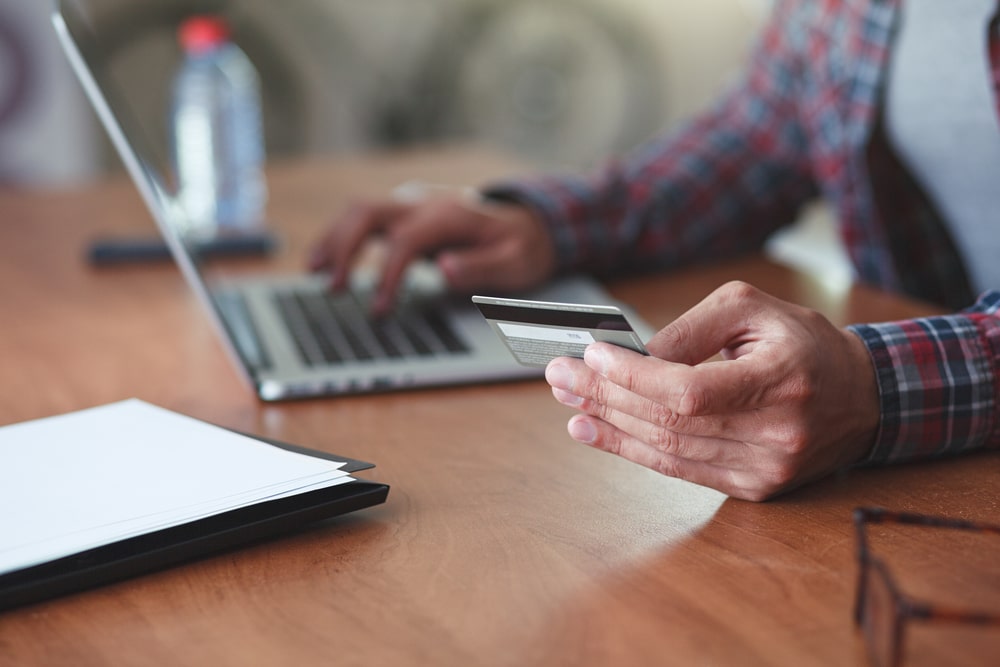 Man holding a credit card and using a laptop for an online purchase.