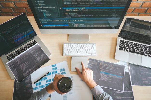 Individual surrounded by laptops and a monitor while typing code