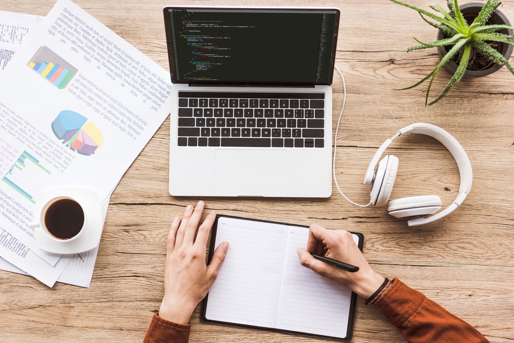 individual writing notes on a notebook in front of a laptop